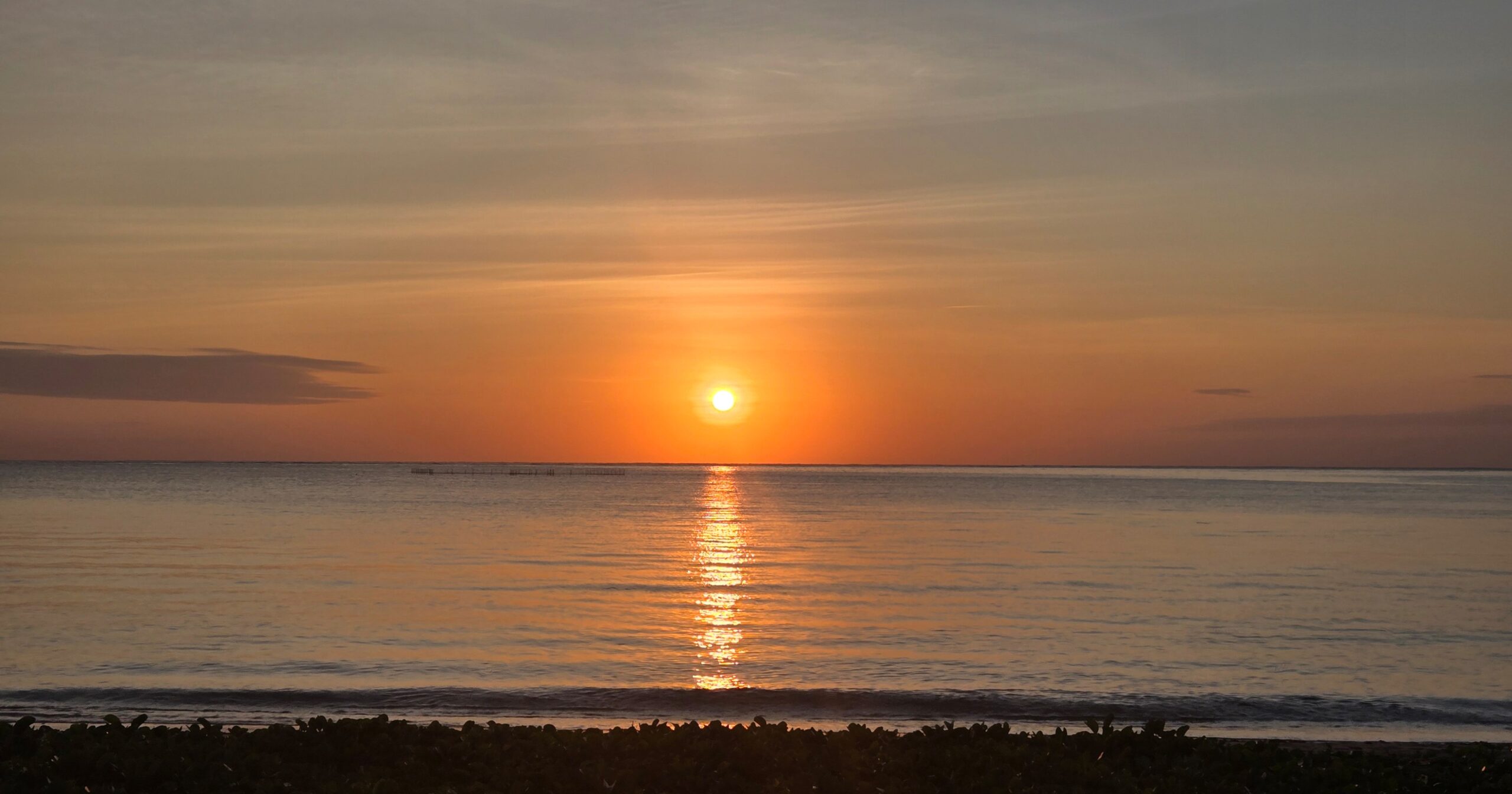 果てしなく広い海に沈む夕陽と、水面に伸びる光の道