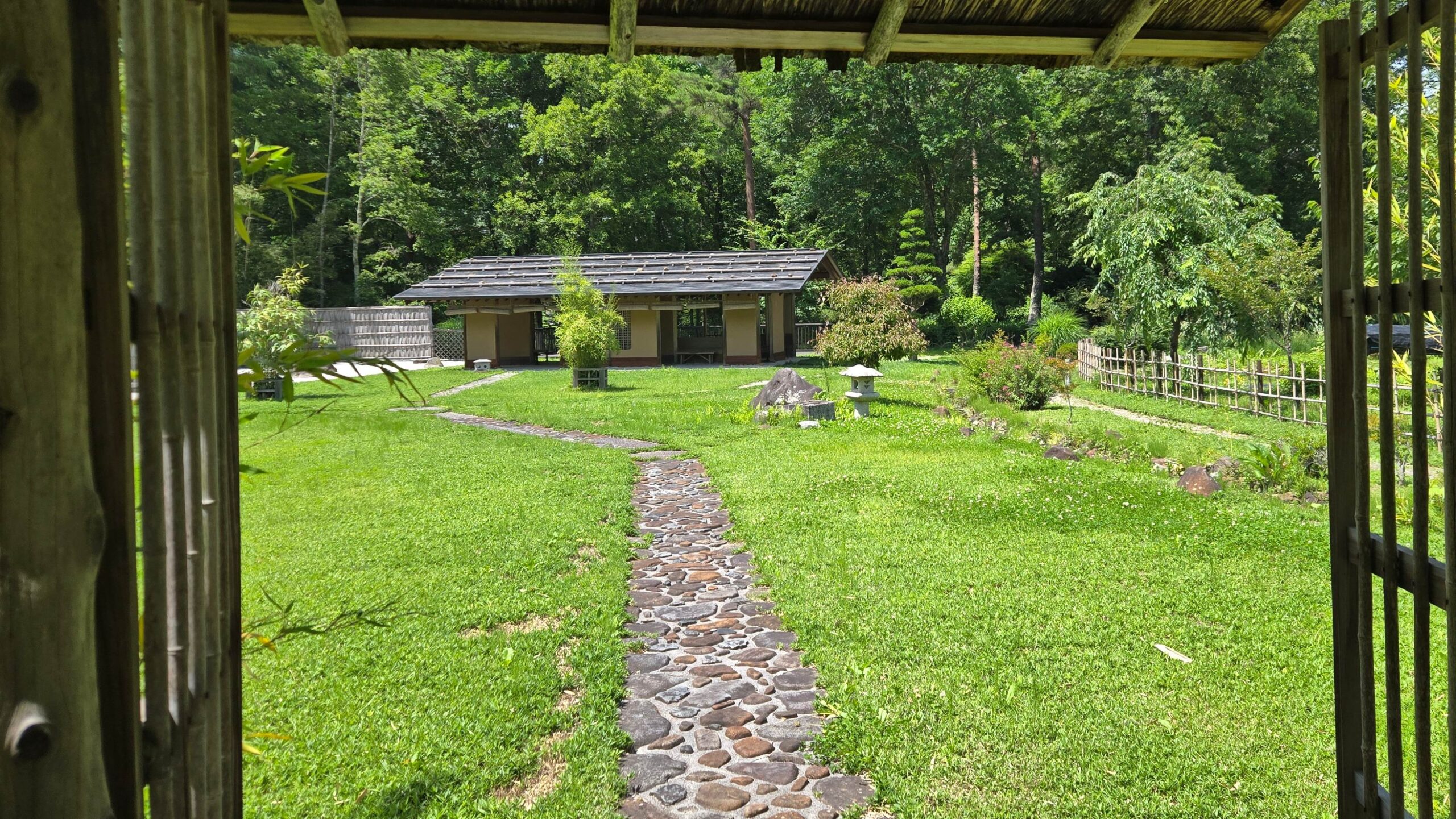 竹垣越しに見える和風庭園と、緩やかに曲がりながら奥の東屋へ続く石畳の小道