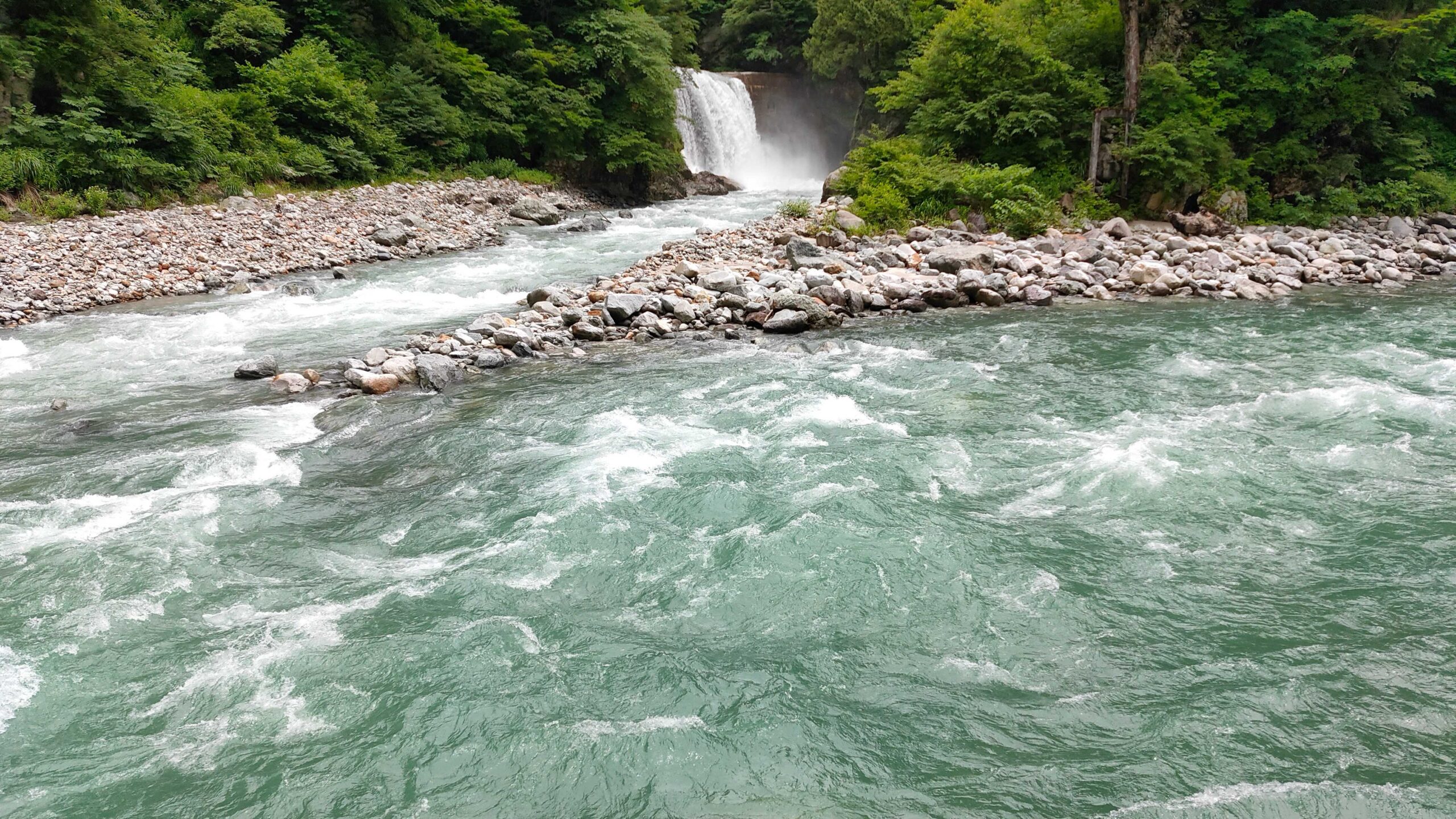 コンクリートの堰から落ちる滝と、中洲で二つに分かれて流れる渓流